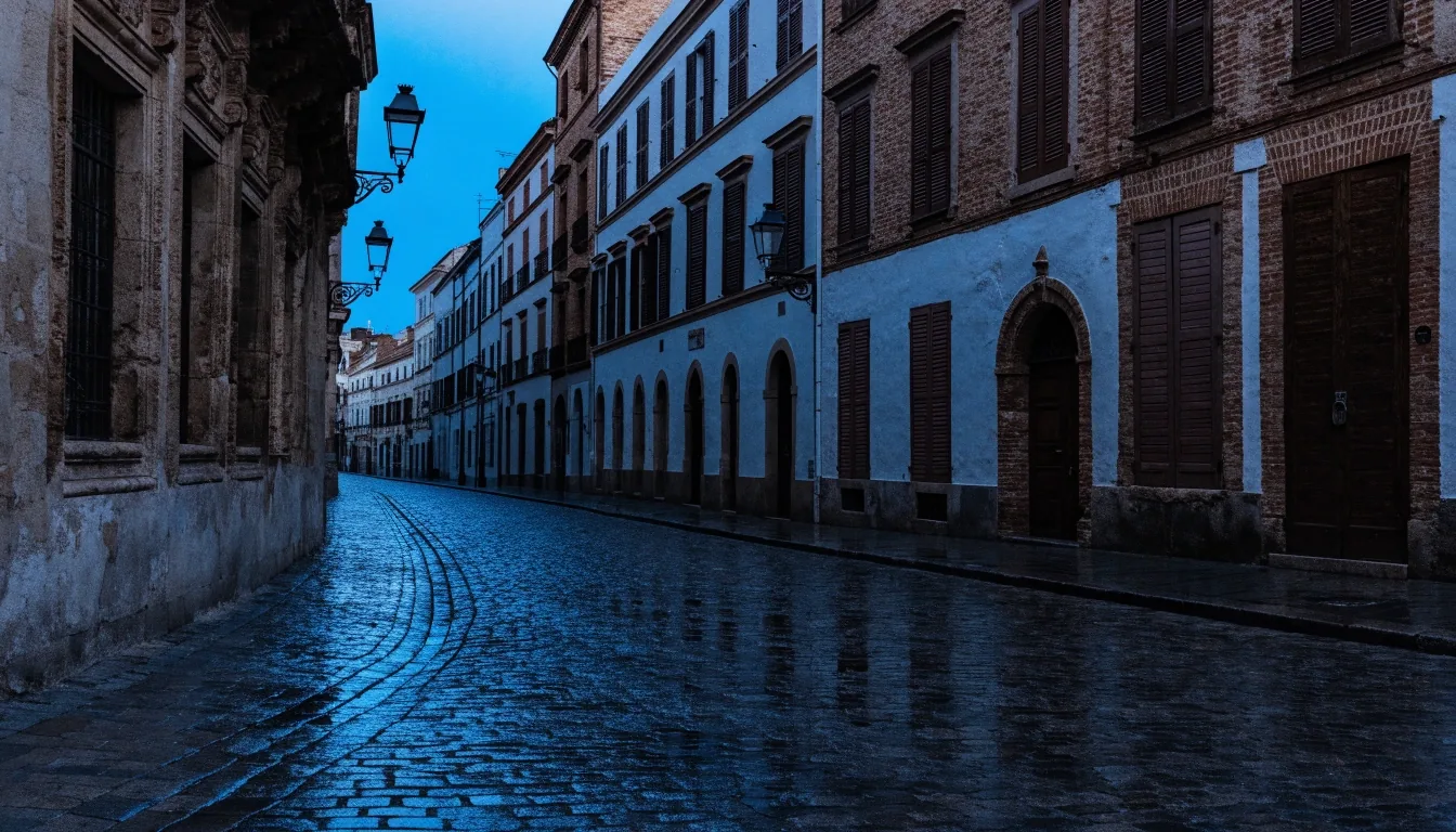 Calle empedrada del centro histórico de Sevilla al atardecer, con persianas cerradas y farolas apagadas